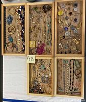 Full view of assortment of costume jewelry items arranged in wooden trays including necklaces, bracelets, rings, brooches, earrings, pins, and pendants.