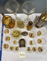 Overview of many vintage carnival glass pieces on display including etched stemware, pitcher, vases, ashtray, and small glasses.