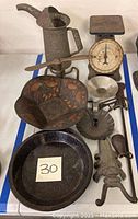 Photo of the collection showing an oil can, balance scale, enamel plate, art deco tray, lobster-shaped jack scraper, and lawn sprinkler.