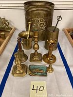 Overview image showing a brass bell, several brass candle holders, a mortar and pestle, a brass fire starter container, and a brass ashtray with ship motif.