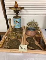 Photo showing the lamp, brass plaque, copper mortar, brass pestle, and other brass trinkets arranged on wooden trays.