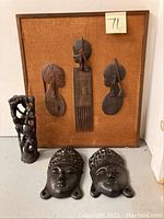 Wooden African mask plaque with three carved figures, wooden figurine statue, and two Asian face wall plaques arranged together.