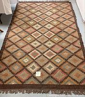 Full view of the handwoven kilim rug showing geometric diamond pattern in earth tones and fringed edges.