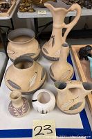 Group shot of six ceramic pieces: three larger beige vessels decorated with feathers in back row, three smaller vases in front