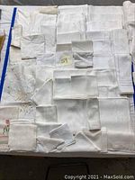 Collection of white linens including tablecloths, napkins, and mats laid out for display showing various embroidered and woven patterns.