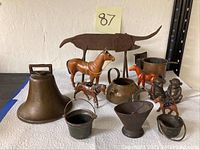 Wide view of all items together showing bronze bell, metal rhino figure, painted wooden horse, copper teapot and small metal buckets