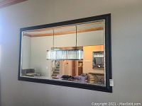 Front view of large rectangular mirror showing reflections of a chandelier and living room interior.