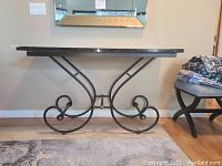 Front view of marble top console table showing black metal scroll base and dark marble surface