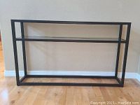 Console table side view showing black metal frame and glass shelf.