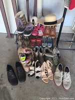 Full view of 15 pairs of assorted shoes and boots including men's, women's, and kids' footwear arranged on and around metal racks with variety of styles and wear conditions.