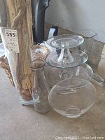 Photo showing multiple clear glass vases of different shapes, a clear glass pedestal cake stand, and a flat round glass tray.