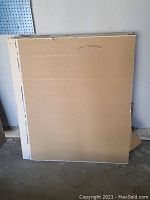 Stack of drywall sheets viewed from front showing front facing sides covered mostly by cardboard.