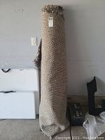 Photo of the rug rolled up against a wall showing woven backside and fringed top.