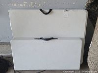 Photo showing two white folding tables stacked side by side with black carry handles.