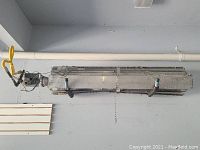 Full view of metal rectangular wall-mounted gas and coil heater with gas valve and wiring attached.