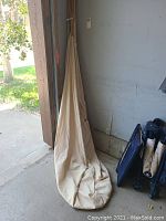 Beige fabric canopy hanging folded against wall with bottom pooled on ground in garage area.