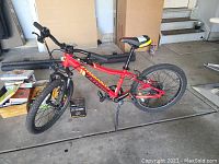 Full side view of the red kids bike showing frame, tires, pedals, and kickstand.