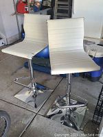 Pair of white barstools with square chrome bases, height adjustment handles and curved back support, some dark marks on fabric.