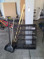 Wide shot showing metal dog exercise pen panels laid flat, wooden walking sticks, broom and dustpan in garage setting.