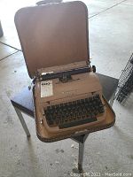 Photo of Remington Quiet-Riter typewriter in open brown case on small black table.