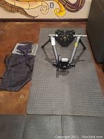 Image showing the CycleOps stationary bicycle trainer placed on a black textured exercise mat, with the carrying bag and sweat guard laid out next to it.
