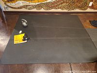 Photo of the 84x72 inch black Pogamat exercise mat laid flat with a kettlebell and informational tag on top.