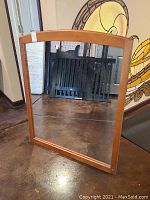 Entire wood framed mirror standing against wall on floor showing front reflective surface and wood frame.