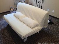 Wide view of futon mattress with white fabric cover and matching pillow in sofa position.