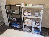 Wide view showing metal and plastic shelving units holding paint cans, stains, grout, and tiles in basement