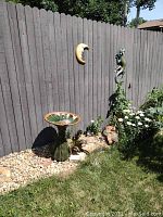 Photo showing ceramic birdbath with garden fence, crescent moon and lizard wall hangings