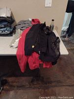 View of the two jackets folded and laid on a table, one black and one red, with visible Ferrari logos on sleeves.