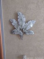 White metal wall decor shaped like large white leaves with texture details against beige wall.