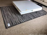 Full view of the IKEA Ransby area rug under a white coffee table, showing its size and striped pattern in shades of brown, grey, and beige.