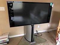 Full view of Samsung TV mounted on metal and glass stand against beige wall.