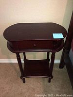 Wood side table front view showing oval top, drawer closed, and lower shelf, dark wood stained with water staining visible on surface.