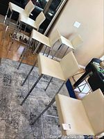 Six matching barstools with chrome legs and cream leather seats and backs on area rug