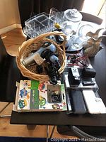 Full view of the lot on a dark table including basket with hair dryer and curling iron, electronic devices, Bose earphones, plastic organizers, and glass decor.