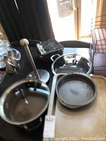 Photo showing Calphalon cookware stainless steel pot and Weber cast iron pans along with other dishware and bowls on table.