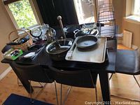 Dining table with attached leaf and six metal chairs with brown leather seats surrounding it. Various household items placed on the table are not included.