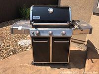 Weber Genesis propane grill front view showing three control knobs, dual doors, and side shelves placed on an outdoor patio.