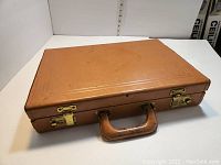 Closed vintage brown leather briefcase-style case with metal clasps and handle showing wear and scuffs.