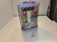 Front and side view of purple plastic bead carousel case containing multiple compartments of small multicolored beads and some visible handmade jewelry pieces inside.