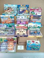 Eleven Chevron Cars toy vehicles in original packaging arranged on a flat surface, showing box designs, vehicle styles, and colorful backdrops in the packaging.