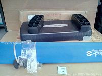Photo showing one black plastic exercise stepper with risers placed on top of its original box, a blue padded mat with Core Body branding partially visible beneath it.