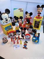 Wide view of entire lot showing clocks, bobbleheads, Pez dispensers, radio, and figurines arranged on a table.