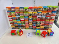 Front view of all 71 Fisher Price Peek a Boo Sensory Blocks stacked in 7 rows. Various colors, textures, and objects inside transparent plastic cubes visible.