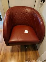Front view of red leather swivel accent chair showing diamond-stitched curved back and cushioned seat.