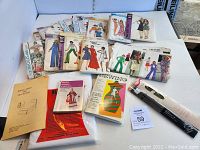 Vintage sewing patterns, books, packaged zippers, and interfacing arranged on a white surface.