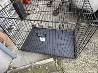 Large black metal dog crate with bottom tray on concrete ground from front angle.