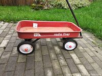 Side view of red Radio Flyer 90 wagon on brick ground showing full profile, red wagon bed, wheels and handle.